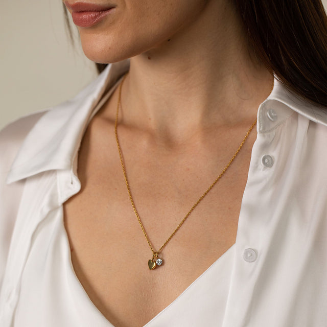 PURELEI Brave Kette in Gold mit Herz- und Zirkonia-Anhänger, elegant getragen zu weißer Bluse, stilvoll feminin.