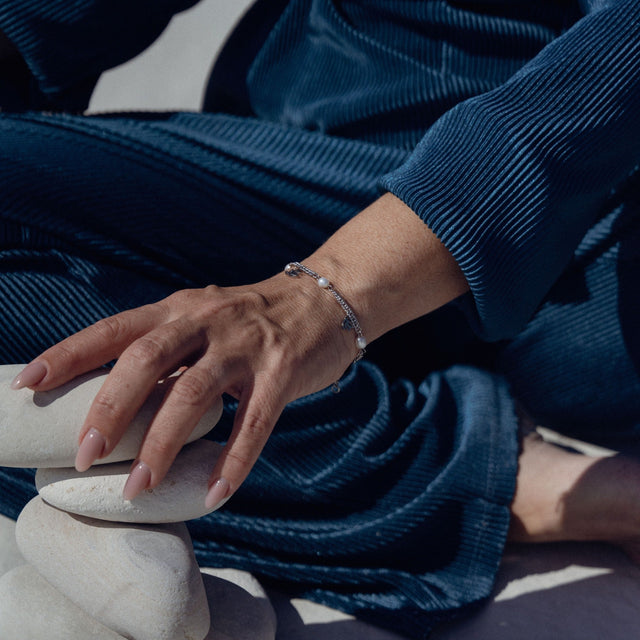 Silbernes Armband mit Perlen, getragen auf einer Hand, umgeben von weißen Steinen – PURELEI.