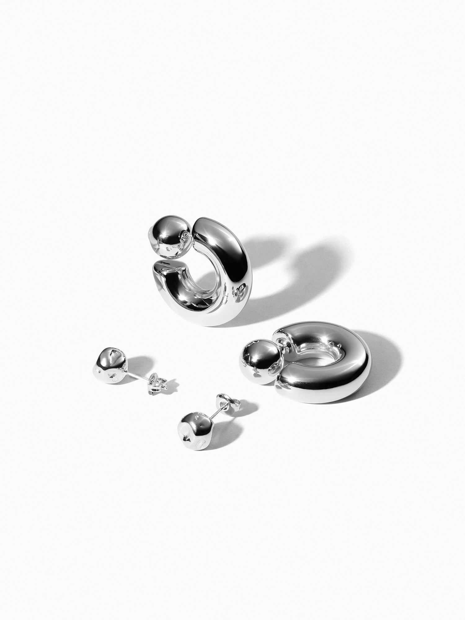 Silberne Creolen und Ohrstecker von PURELEI, glänzend und modern, elegant inszeniert.