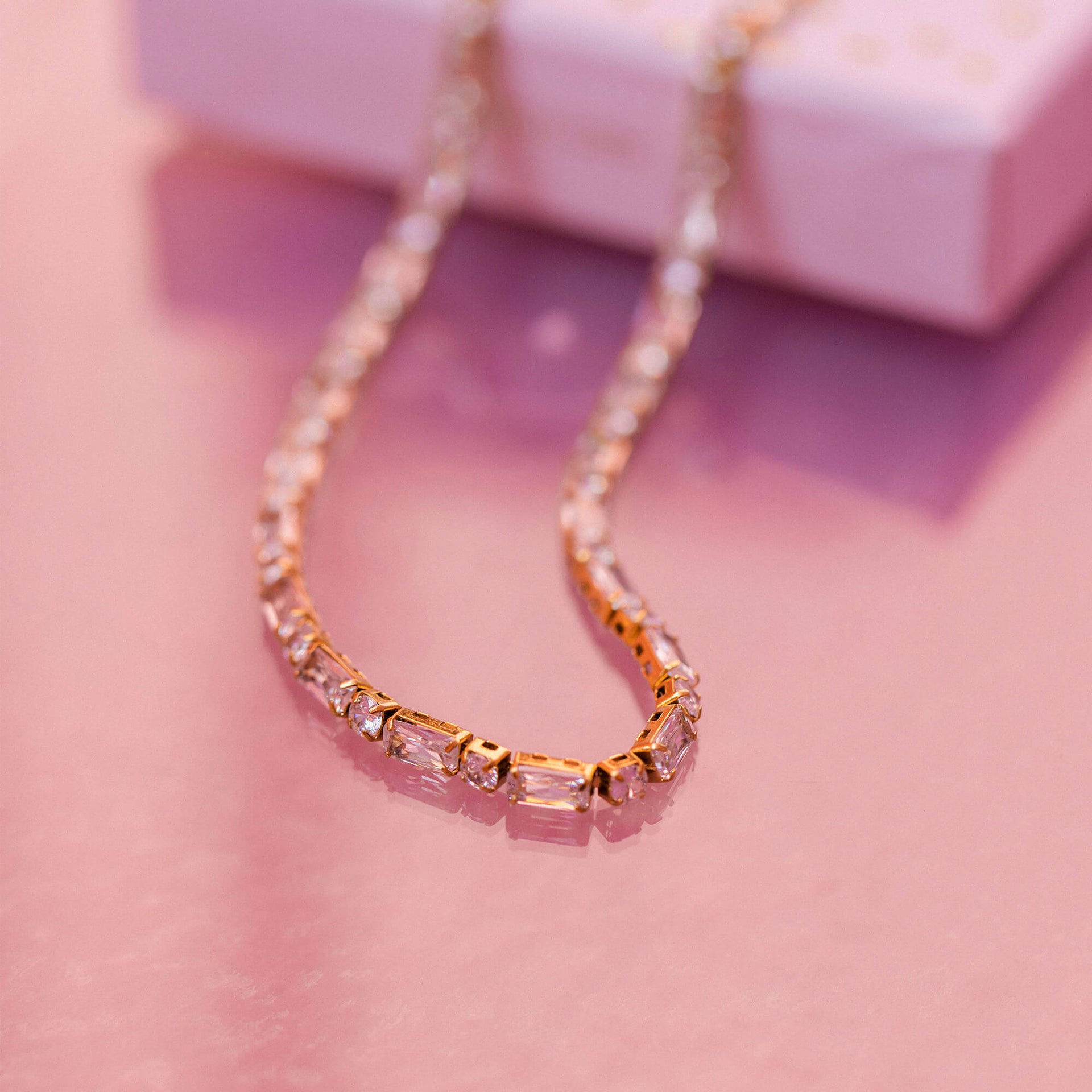 Roségoldene Kette mit funkelnden Steinen, elegant auf sanftem Untergrund, PURELEI.