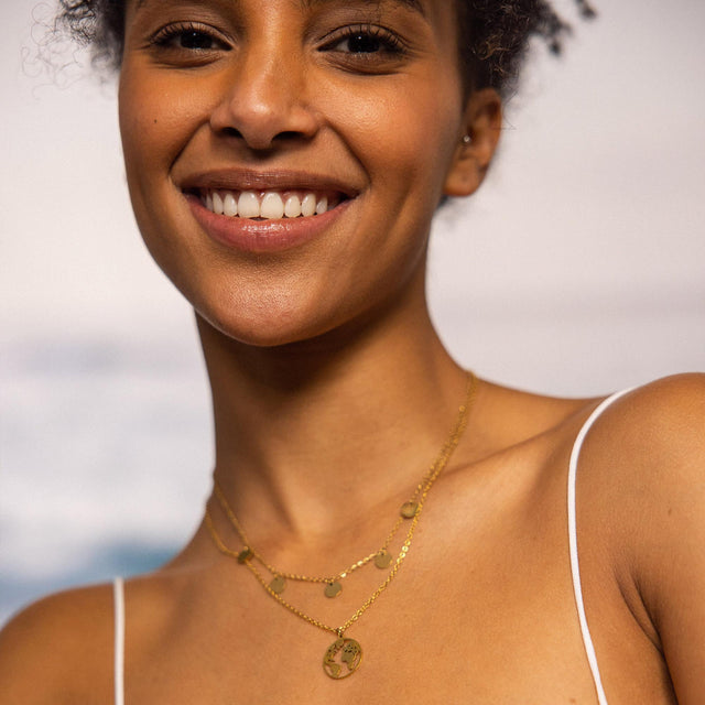 Goldene PURELEI Kette mit Anhängern, getragen in warmem Sonnenlicht.