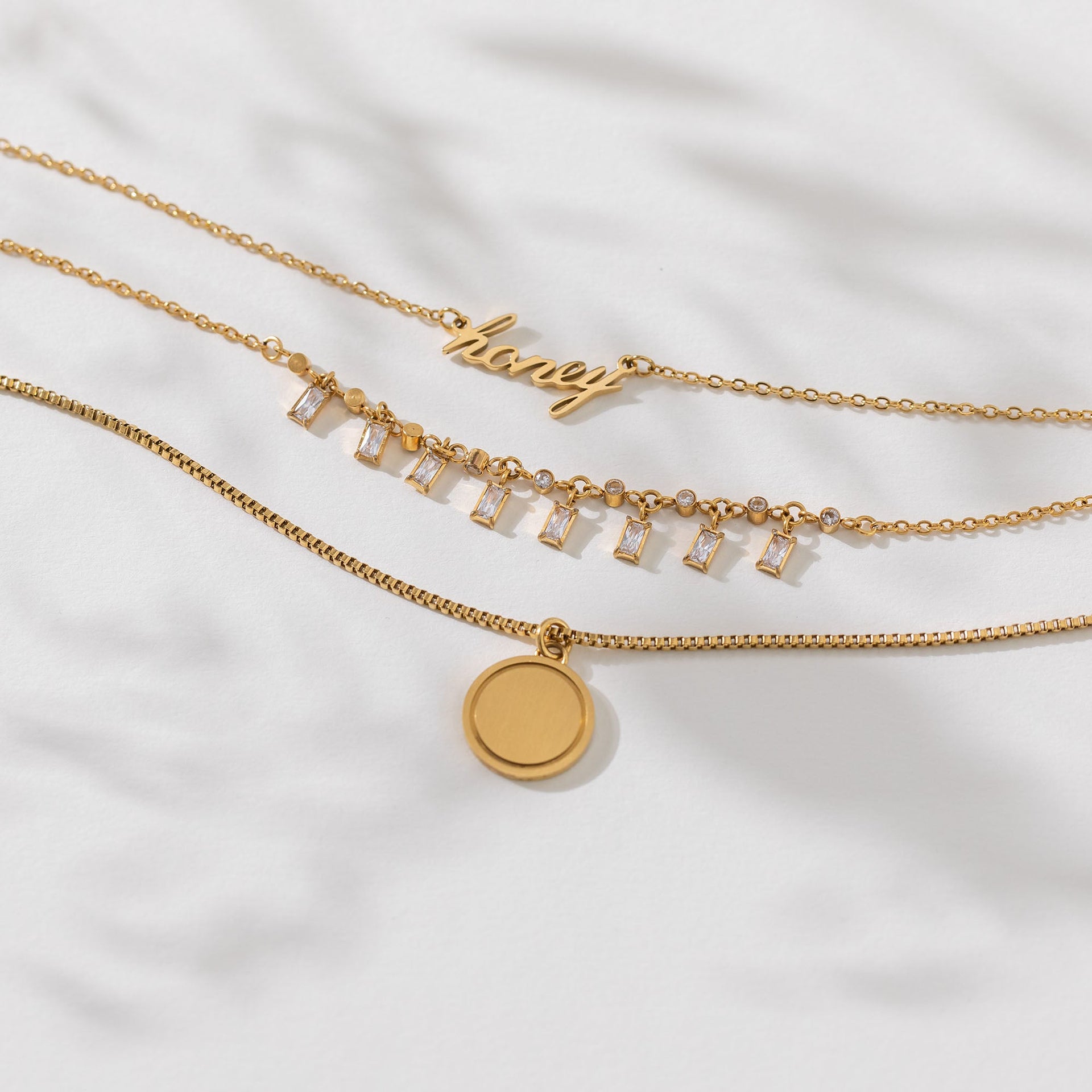 PURELEI Honey Kette aus 18K Gold Edelstahl mit geschwungenem Schriftzug, elegant und feminin auf weißem Leinen.