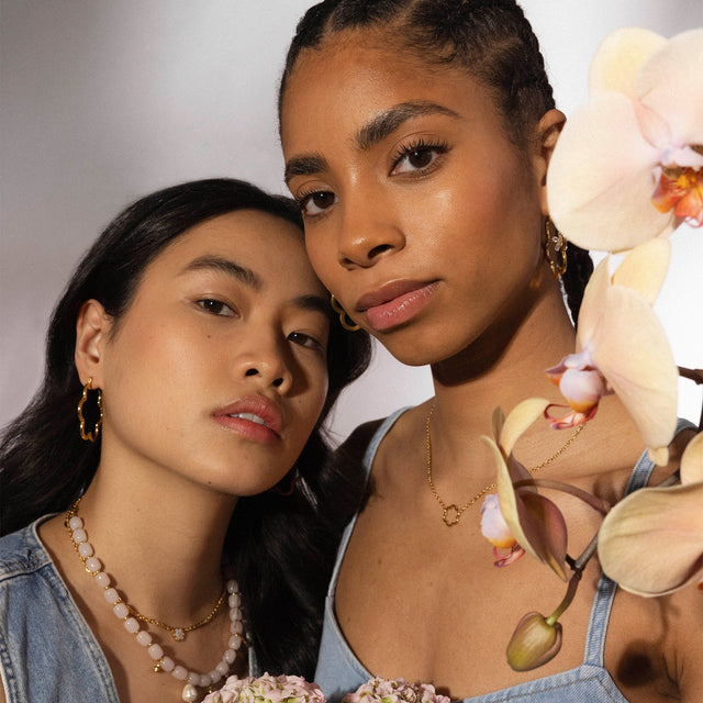 Zarte PURELEI Schmuckstücke in Roségold und Perlen, getragen von zwei Frauen mit blühendem Hintergrund.