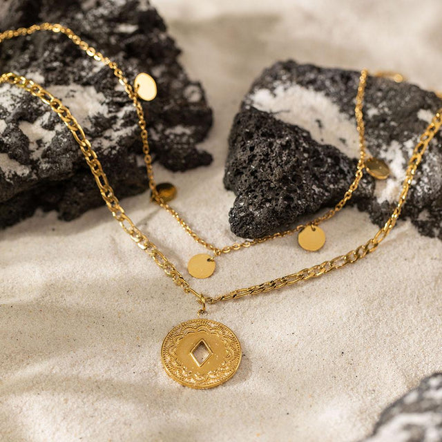 PURELEI Lolani Kette aus 18K vergoldetem Edelstahl mit gemustertem Coin-Anhänger auf Sand und Lavastein