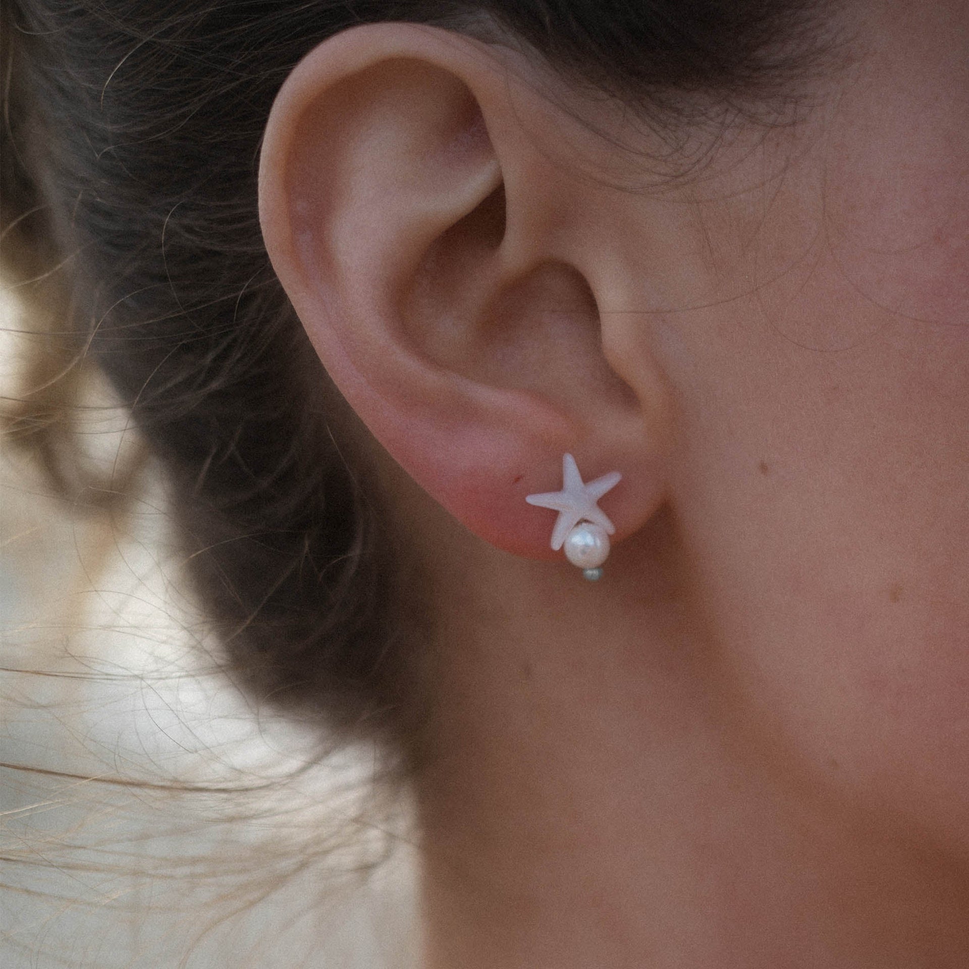 Weißes Sternenohrring-Design mit Perle, getragen von PURELEI, inspiriert von der Meereswelt.