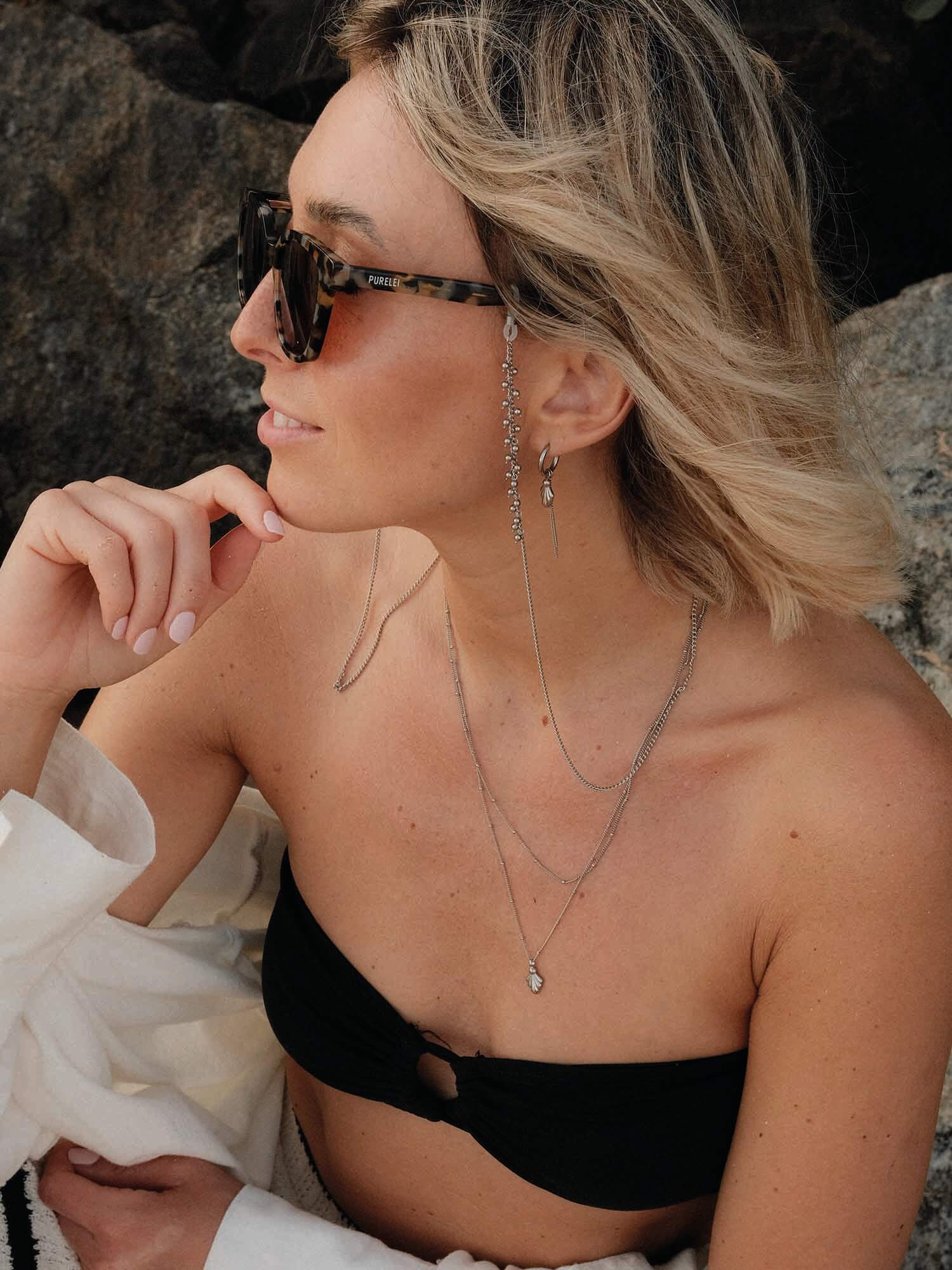 Silberne Ketten von PURELEI, elegant und leicht, getragen mit schwarzem Oberteil, entspannte Strandstimmung.