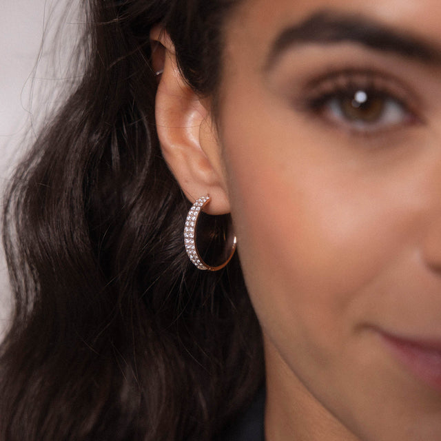 Roségoldene Creolen mit funkelnden Steinen, getragen mit sanftem Lächeln, PURELEI.