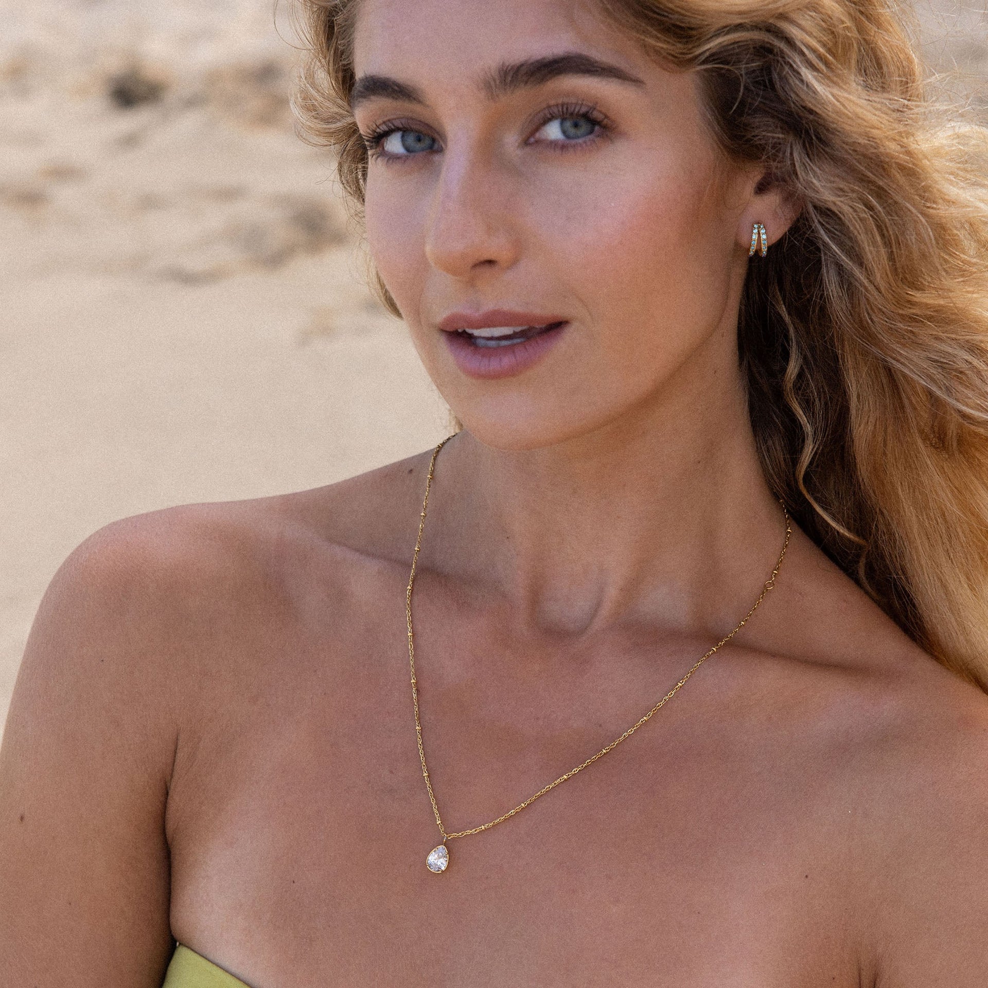 PURELEI Felice Kette mit vergoldeter Edelstahlkette und weißem Zirkonia-Tropfen vor Strandkulisse getragen