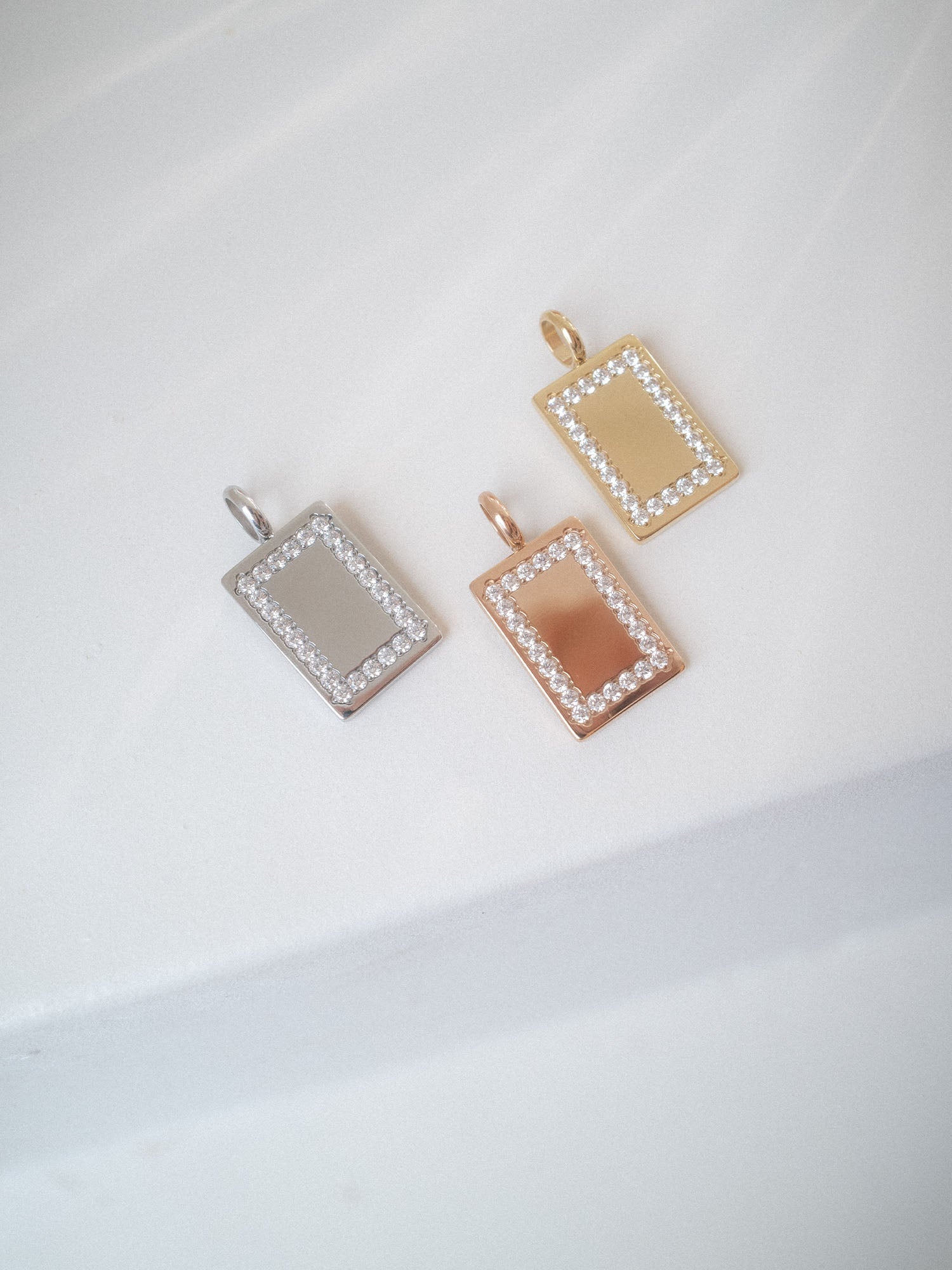 Glimmer Charm in Gold, Silber und Roségold mit Zirkonia-Rahmen, elegant auf hellem Hintergrund, PURELEI.