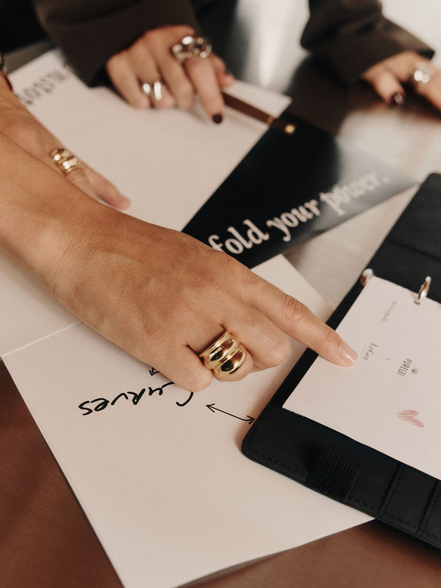Silberne Ringe von PURELEI auf einer Hand, umgeben von Notizen und einem schwarzen Ordner.