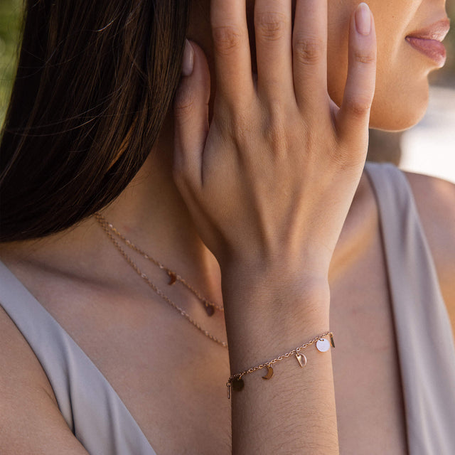 Goldenes Armband mit Anhängern, getragen an zartem Handgelenk, PURELEI Stil.