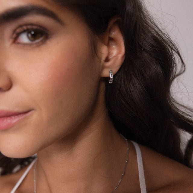 Silberne Creolen von PURELEI, elegant und modern, getragen am Ohr mit sanfter Beleuchtung.