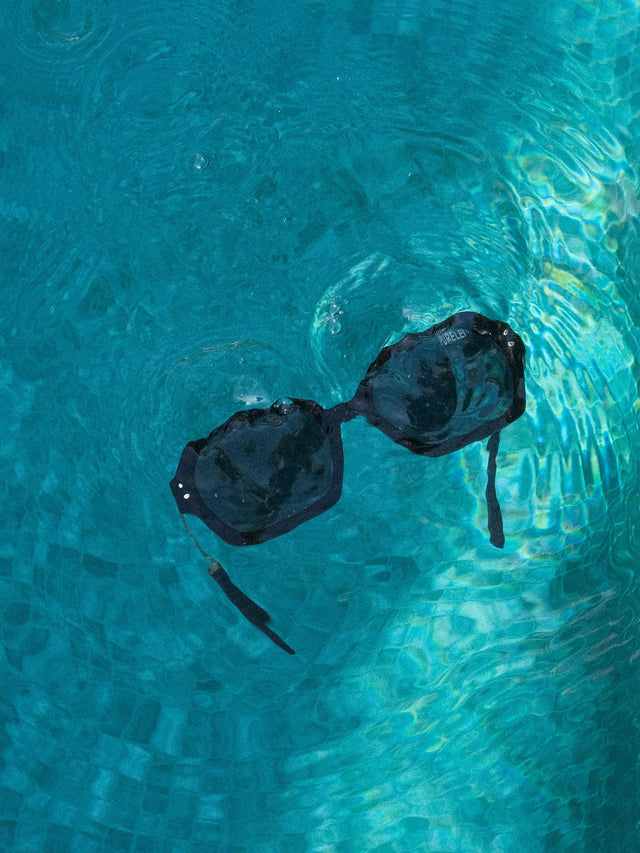 Coastal Core Sonnenbrille von PURELEI in Schwarz mit goldenen Details, wasserfest und stylish im klaren Wasser schwebend.