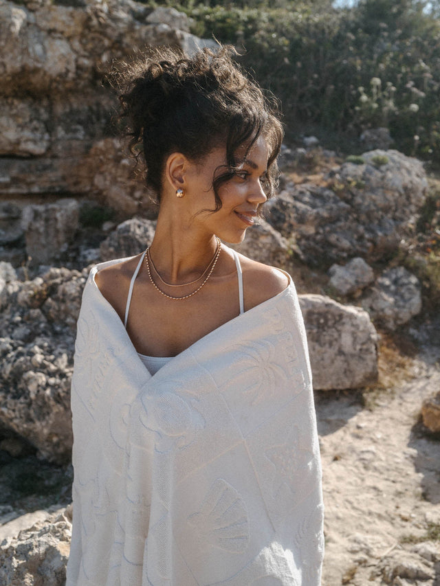 Beige Baumwoll-Jacquard Beach Towel Treasure mit Wellen- und Muschelmotiven, getragen am sonnigen Strand, PURELEI