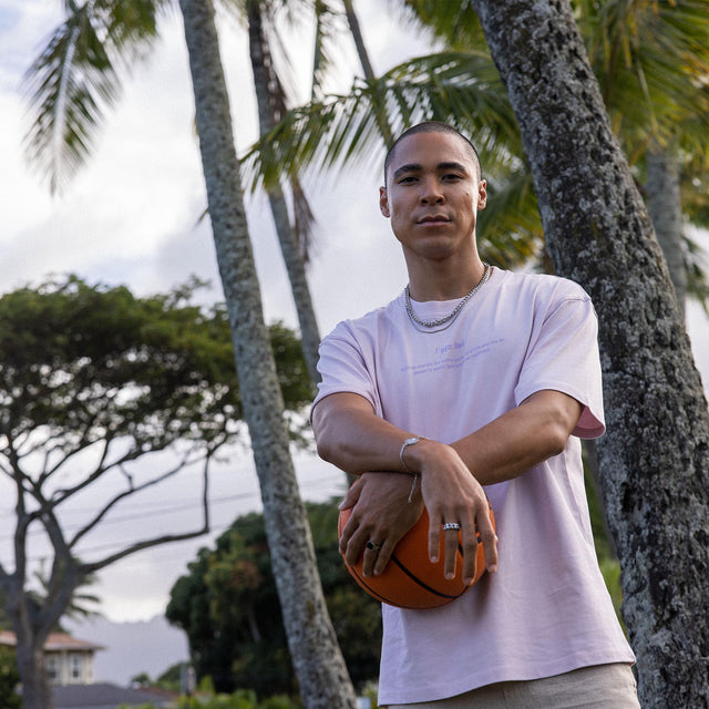 Mann mit Basketball, trägt PURELEI Schmuck, umgeben von Palmen, entspannte tropische Stimmung.