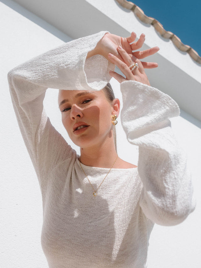 Feminine PURELEI Schmuck in Gold, getragen mit einem weißen Oberteil, strahlende Sommerstimmung.