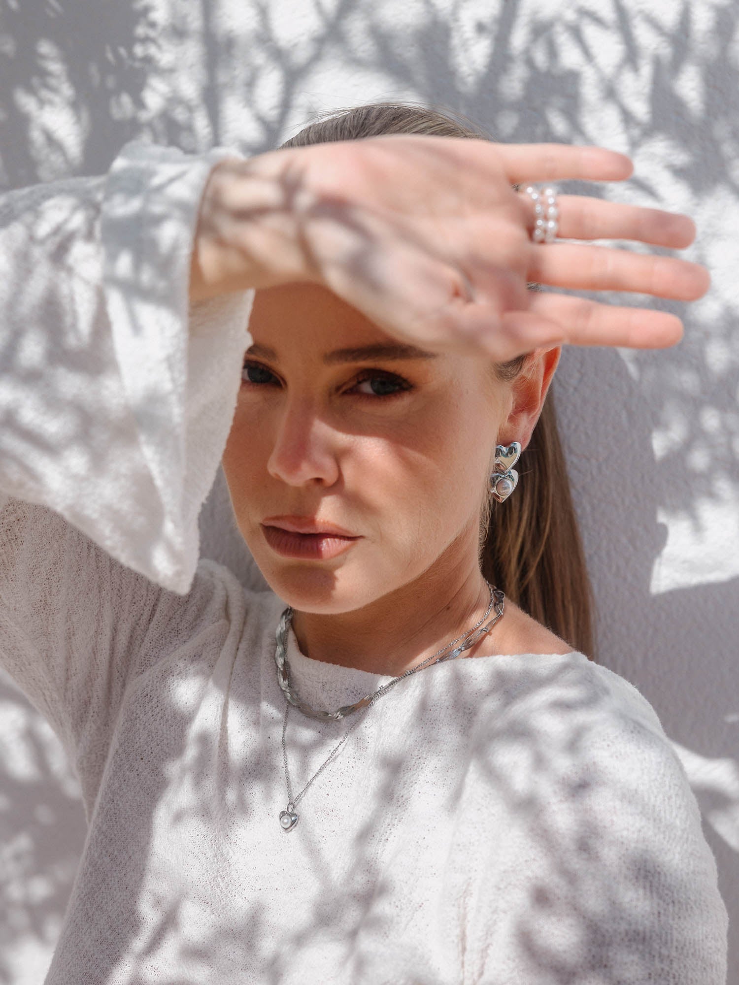 Silberne Ohrringe und Kette von PURELEI, elegant im Sonnenlicht mit Schattenmustern.