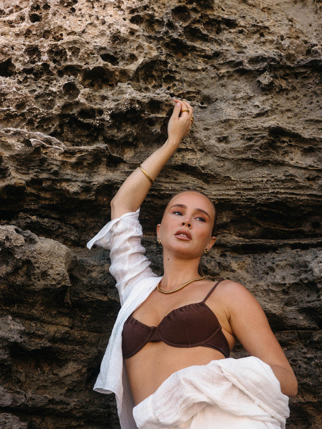 Brauner Bikini mit eleganter Kette, umgeben von natürlicher Felslandschaft – PURELEI Aloha-Vibes.