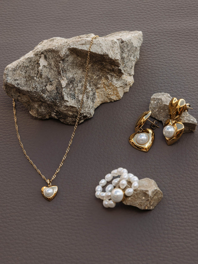 Silberne Herz-Kette und Ohrringe mit Perlen, PURELEI, auf grauem Stein präsentiert.