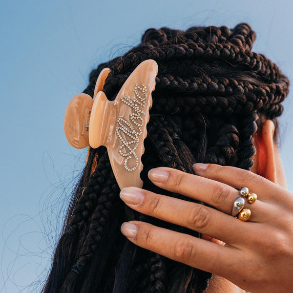 Aloha Haarklammer von PURELEI in Beige mit glitzerndem Schriftzug aus Kunststoff und Strasssteinen am geflochtenen Haar