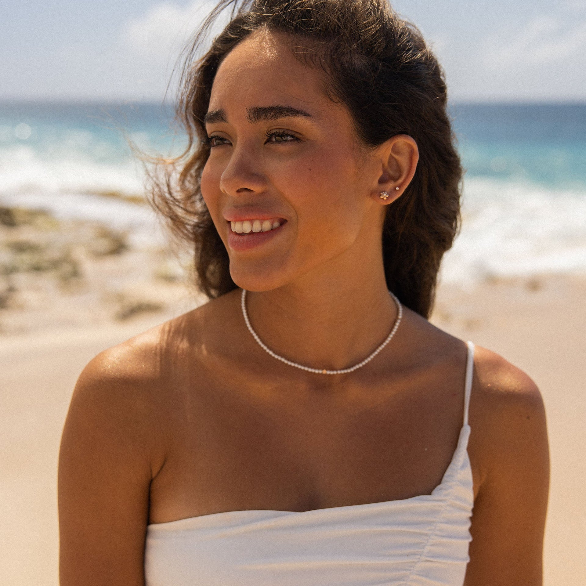 Zarte Perlenkette von PURELEI, strahlend weiß, am Strand getragen, mit tropischer Leichtigkeit.
