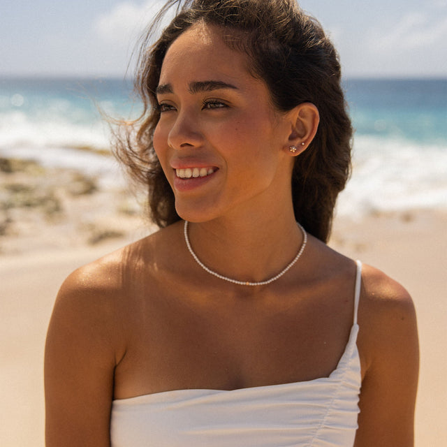 Zarte Perlenkette von PURELEI, strahlend weiß, am Strand getragen, mit tropischer Leichtigkeit.