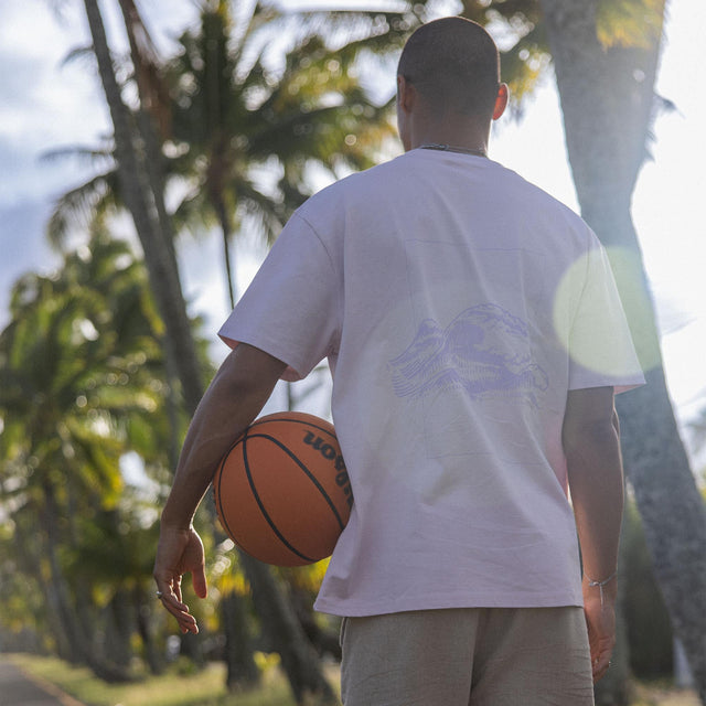Weißes T-Shirt mit lässigem Design, getragen in tropischer Umgebung, PURELEI-Style.