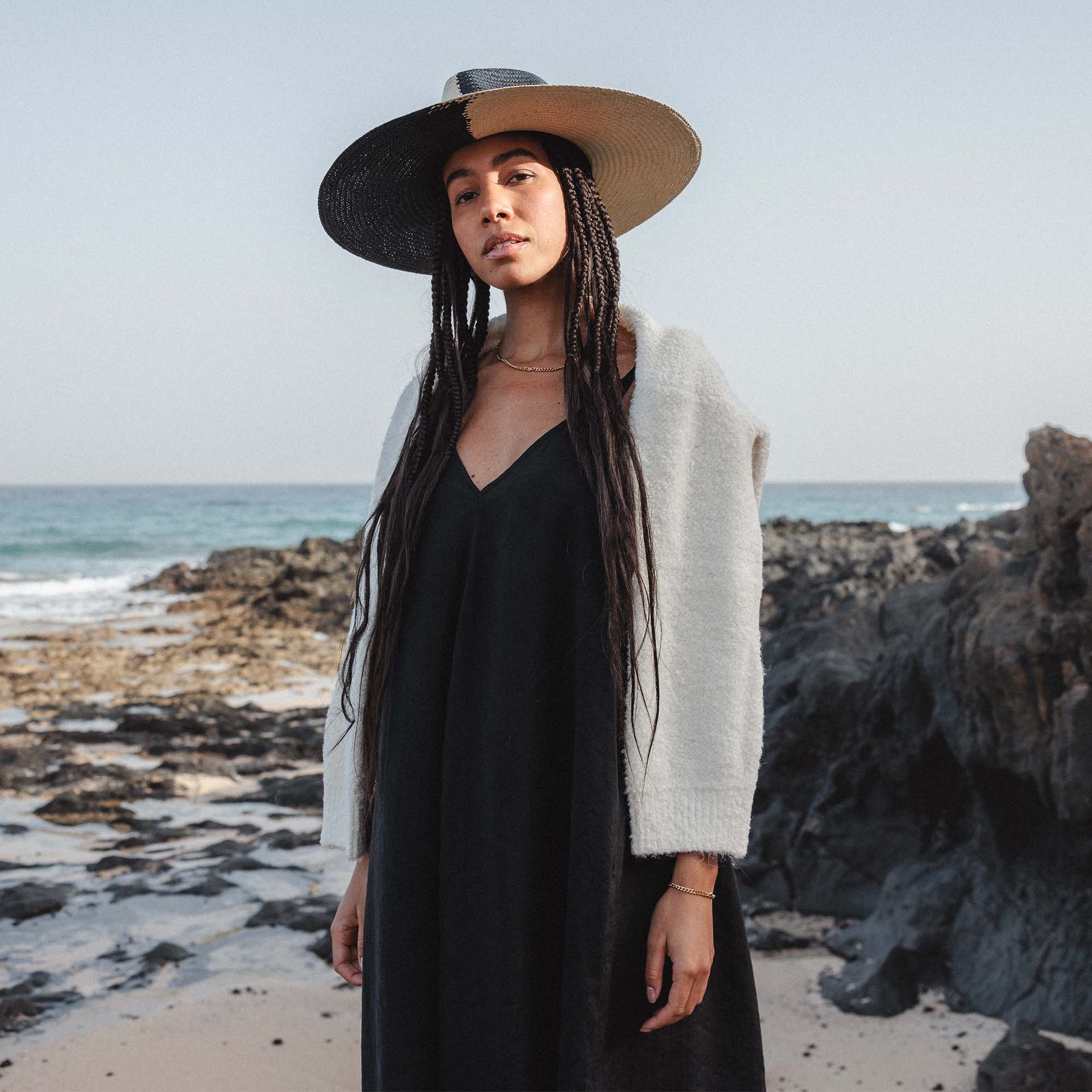 Frau in schwarzem Kleid und weißer Jacke am Strand, PURELEI inspiriert.