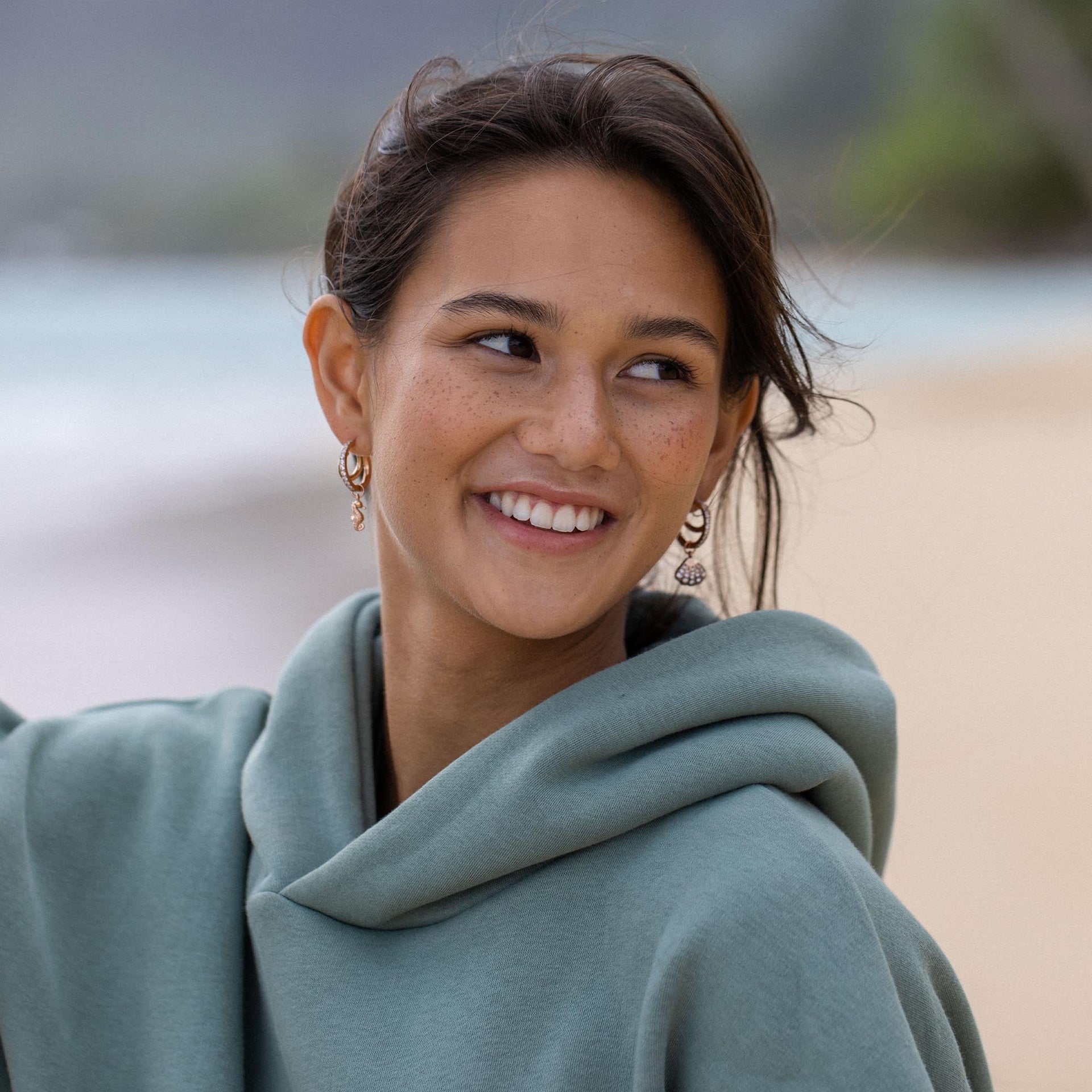 Feminine Ohrringe aus Silber, getragen von einer lächelnden Frau in einem Hoodie, PURELEI Stil.