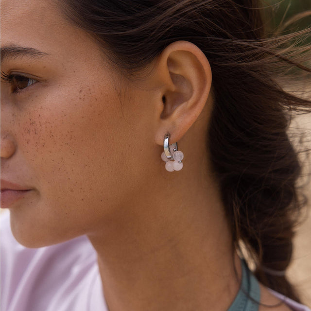 Silberne Creolen mit blütenförmigem Anhänger, getragen von einer Frau, PURELEI.