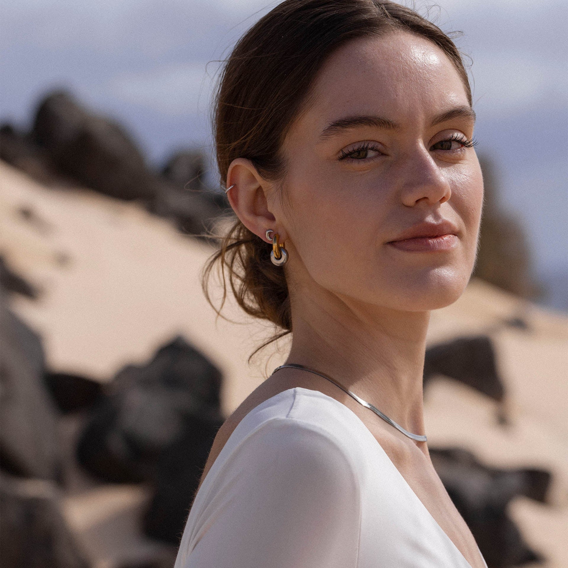 Silberne Creolen und Halskette von PURELEI, elegant und modern, vor natürlichem Hintergrund.