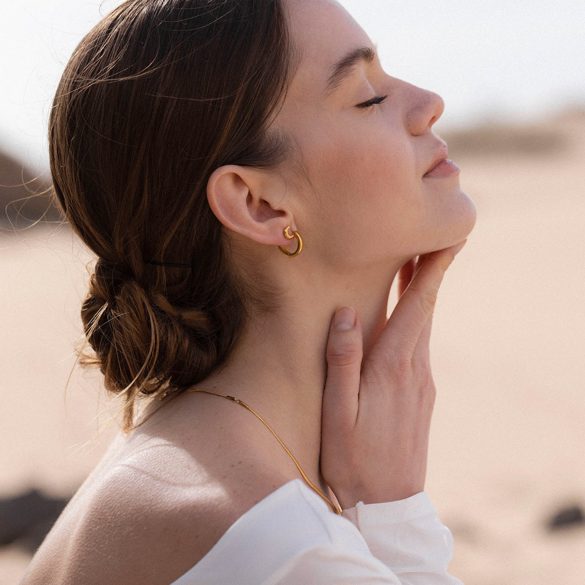 Goldene Creolen und zarte Kette von PURELEI, elegant und feminin, in warmem Licht.