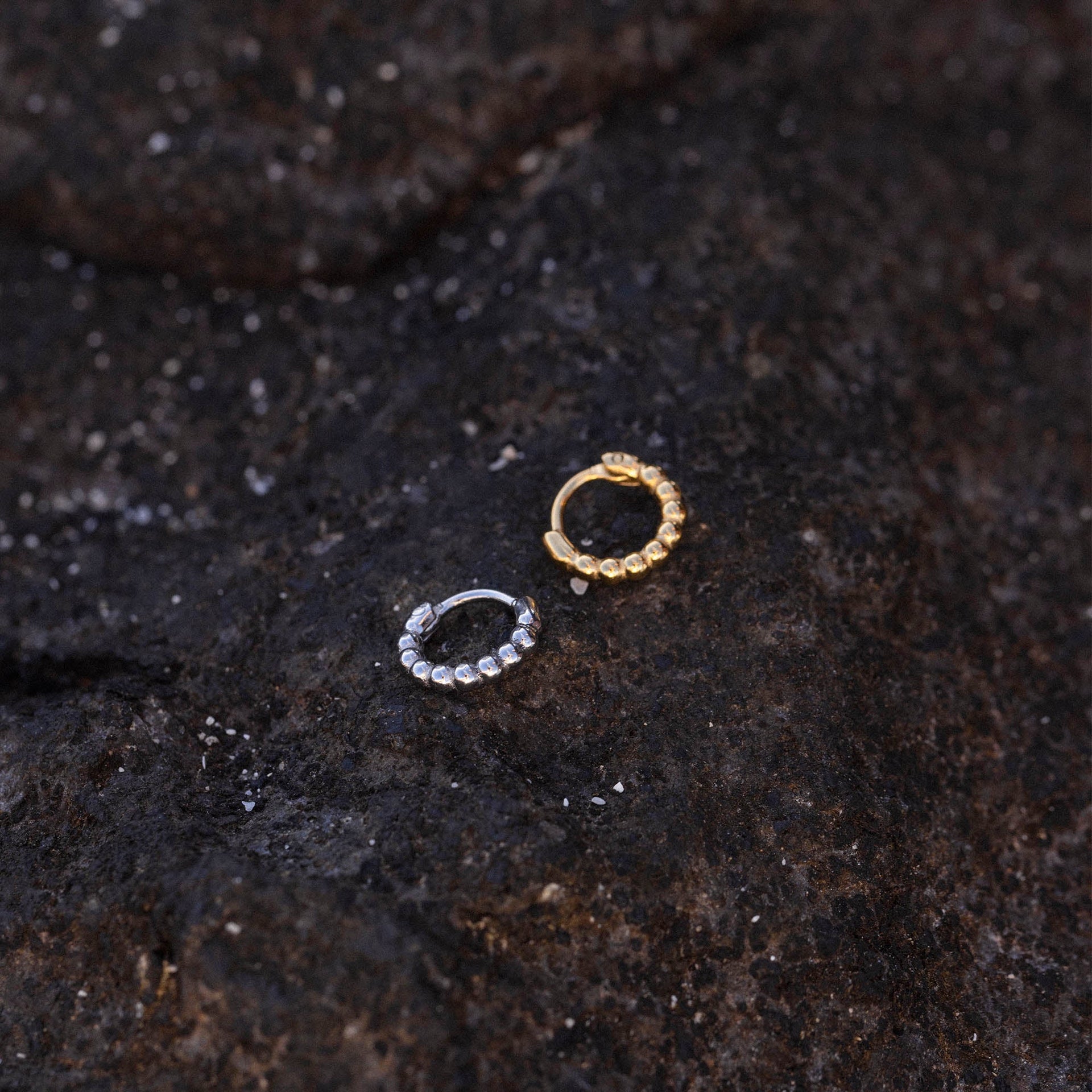 PURELEI Spherical Piercing in Gold und Silber mit kugeligem Design auf dunklem Lavagestein, elegant und nickelfrei