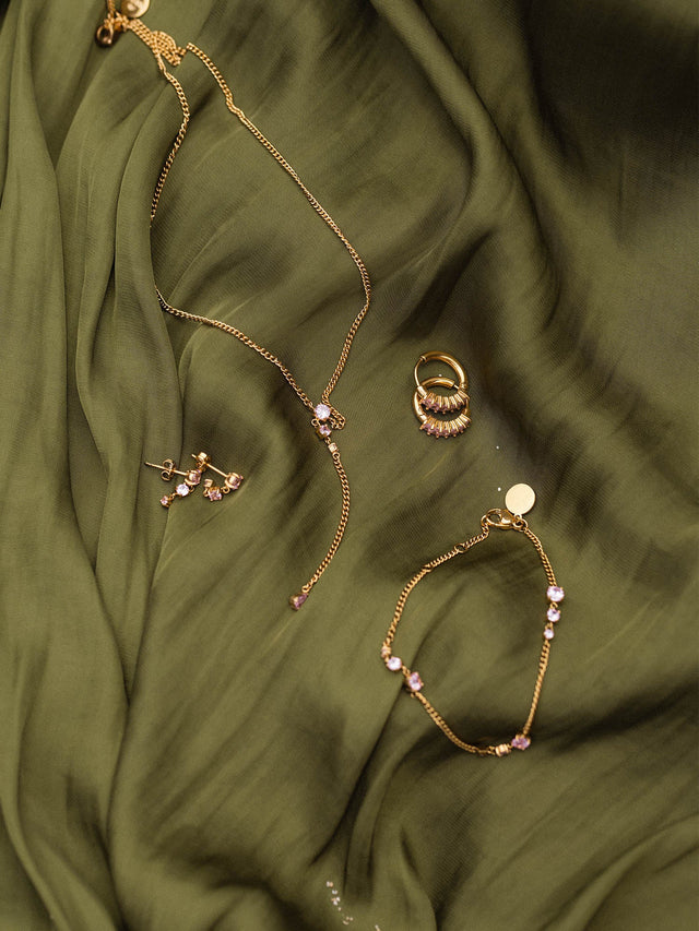 Goldene PURELEI Schmuckstücke auf sanftem, olivgrünem Stoff, elegant und feminin.