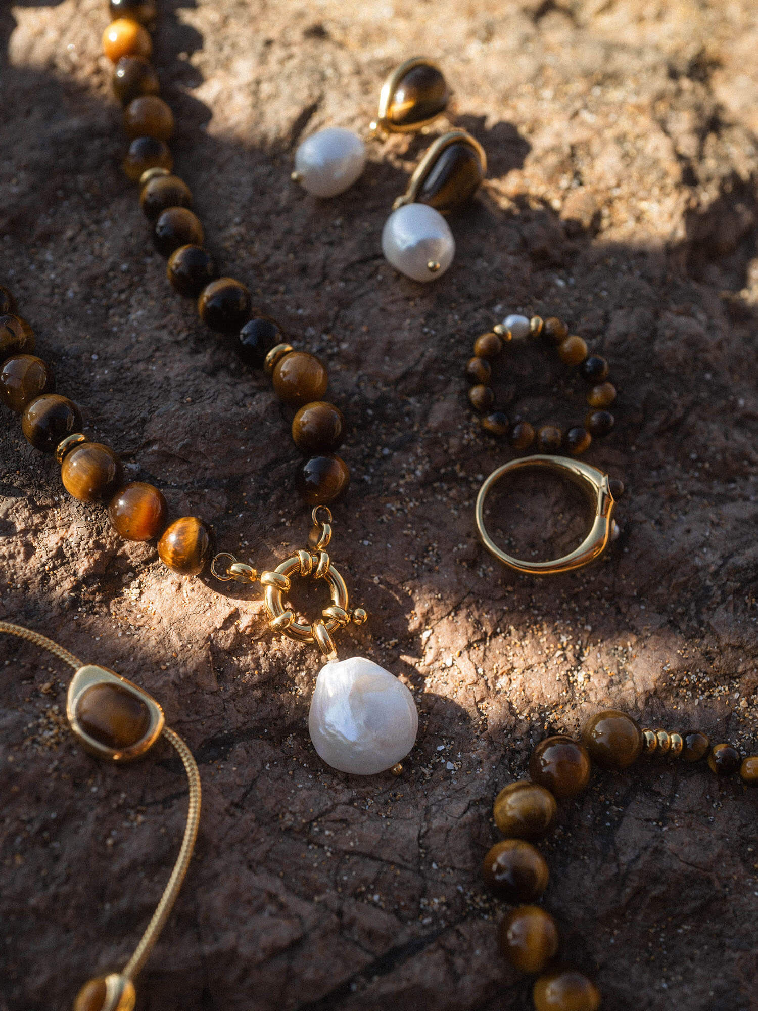 Goldene Schmuckstücke mit Tigerauge und Muschel, inspiriert von PURELEI, auf dunklem Untergrund.