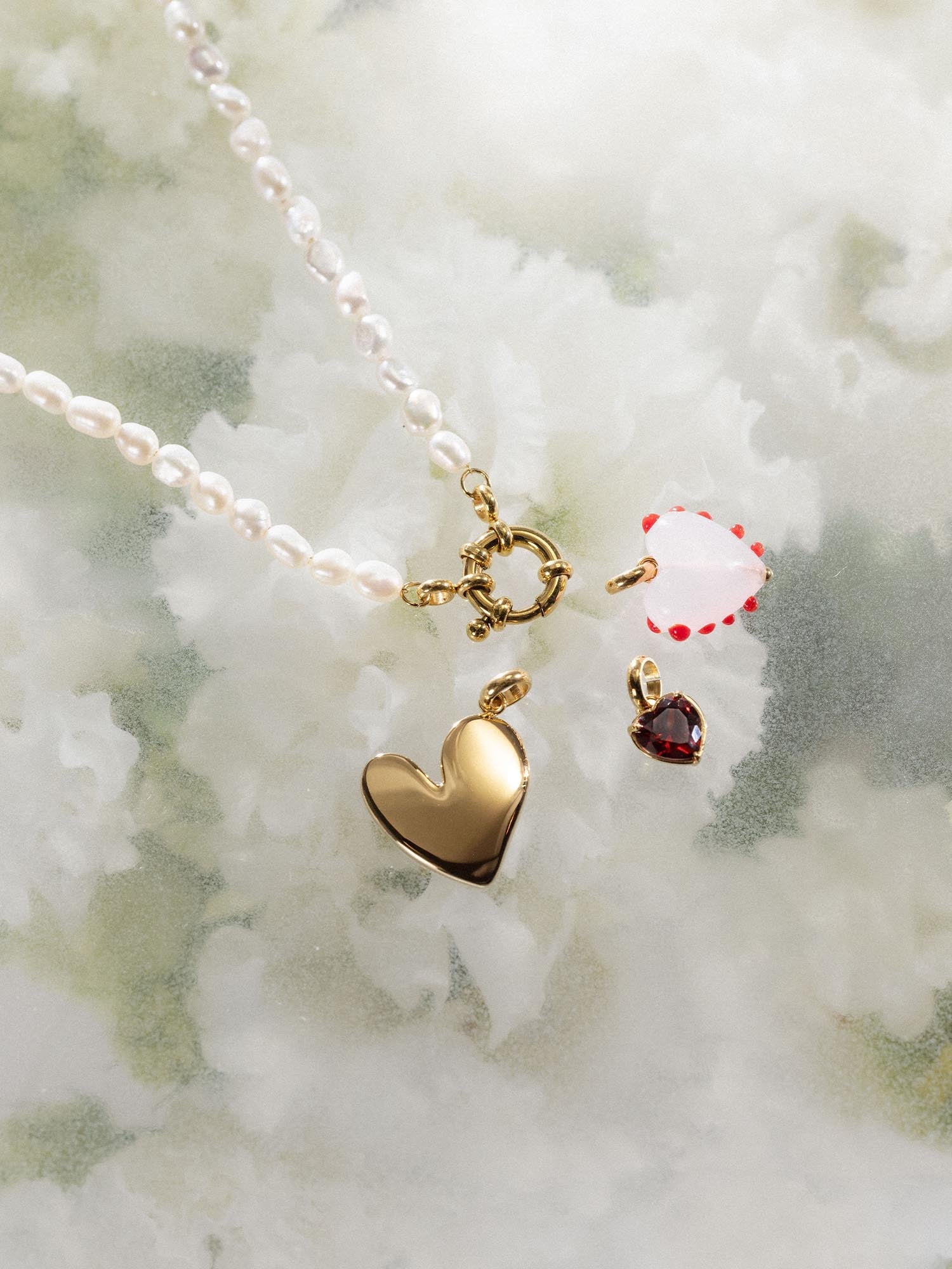 Heart Of Glass Charm von PURELEI, rosafarbenes Glasherz mit roten Punkten und goldener Fassung, elegant und feminin.