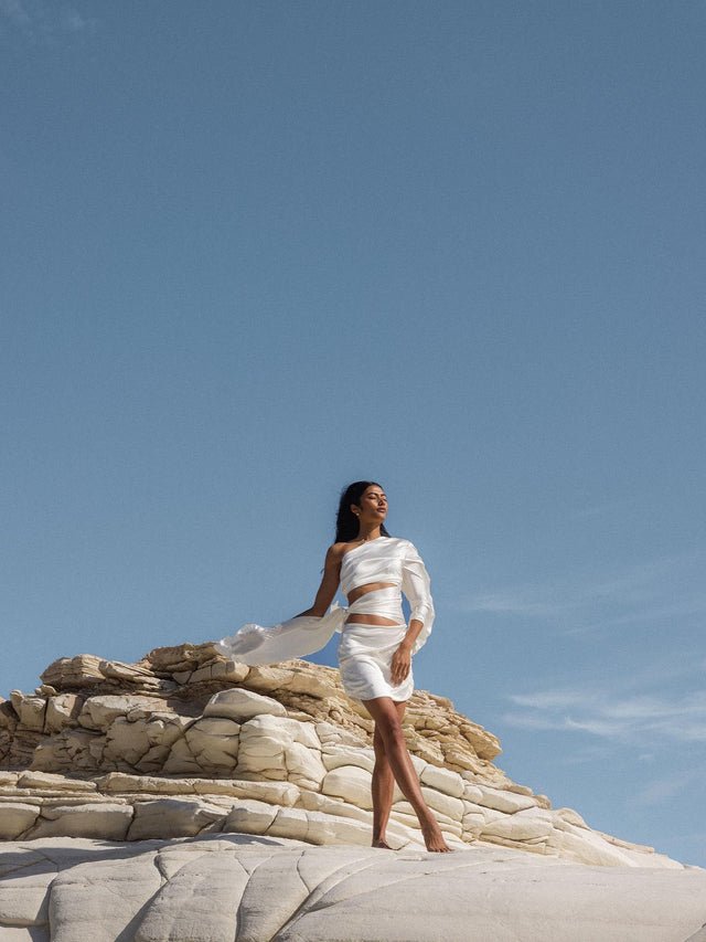 Aquarius Letter Charm aus rosévergoldetem Edelstahl, minimalistisch, getragen vor hellem Fels und klarem Himmel, PURELEI.