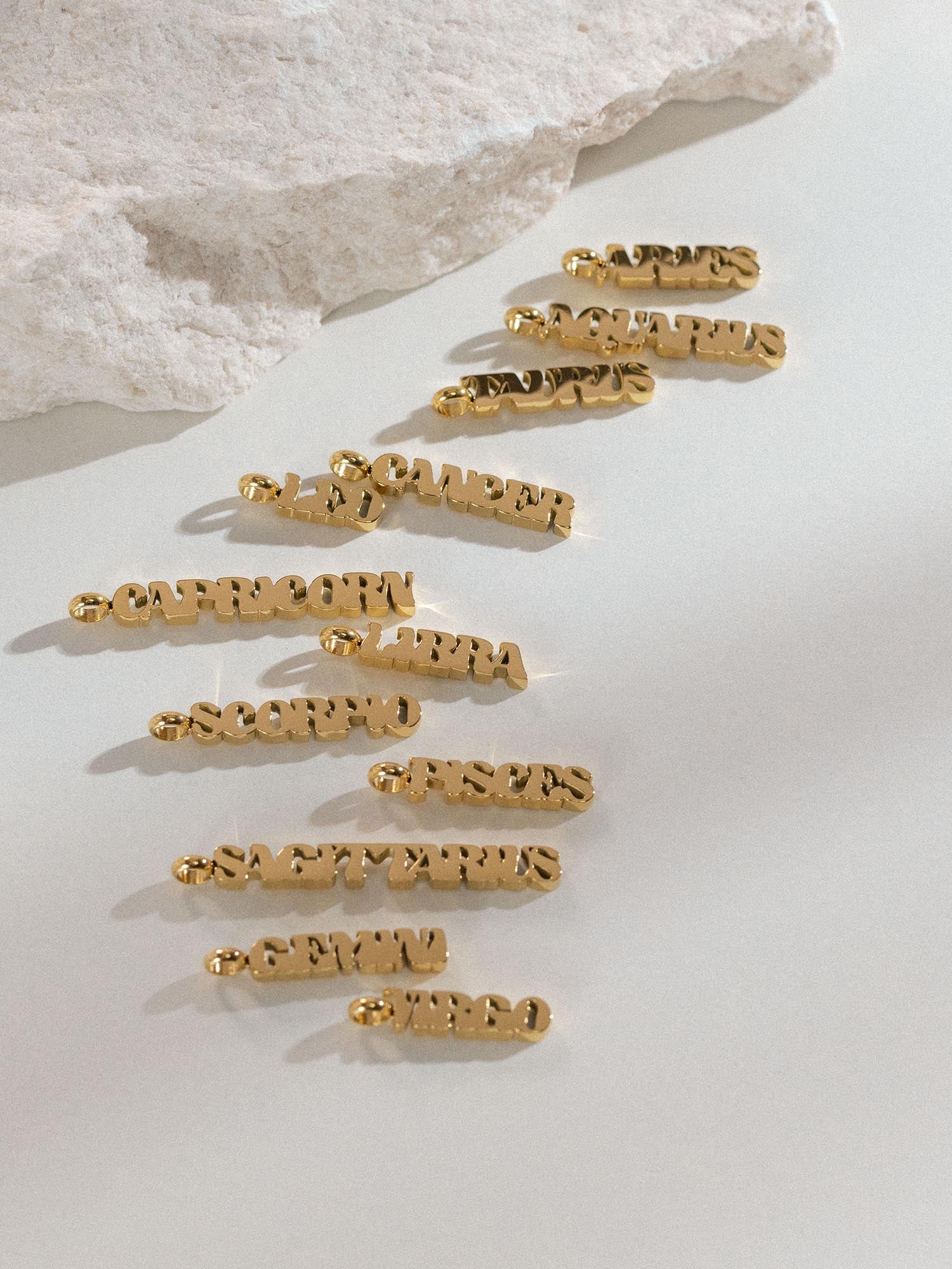 PURELEI Aquarius Letter Charm in 18K vergoldetem Edelstahl, fein gearbeitet mit klarem, modernem Design auf hellem Untergrund.