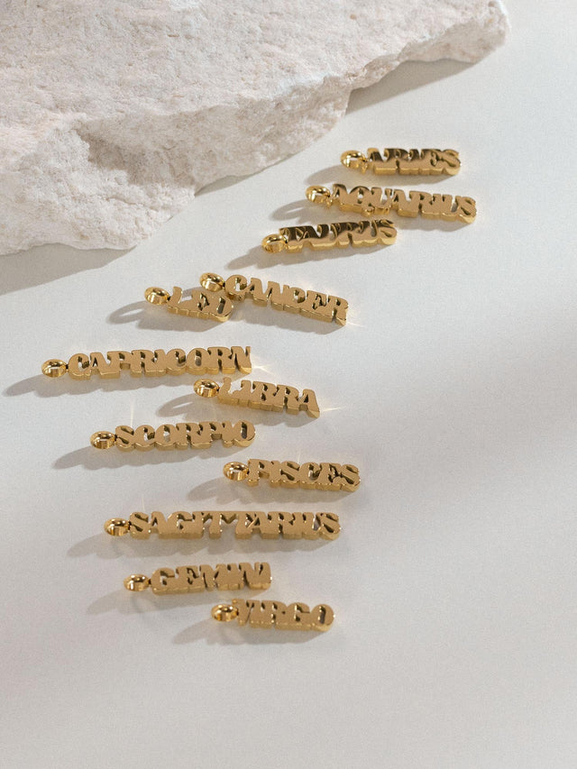 PURELEI Aquarius Letter Charm in 18K vergoldetem Edelstahl, fein gearbeitet mit klarem, modernem Design auf hellem Untergrund.