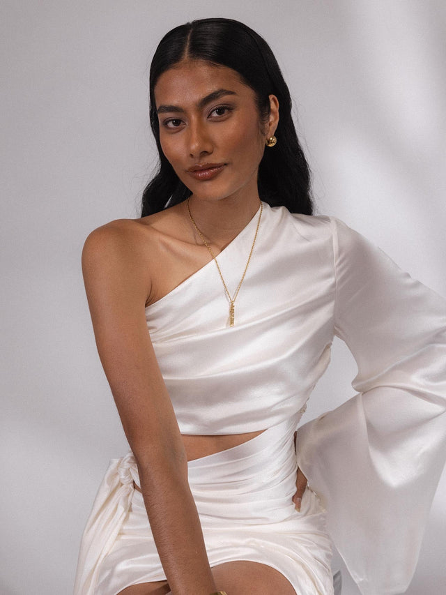 Goldener PURELEI Aquarius Letter Charm an filigraner Kette, elegant getragen zu weißem Satinoutfit, feminin und modern.