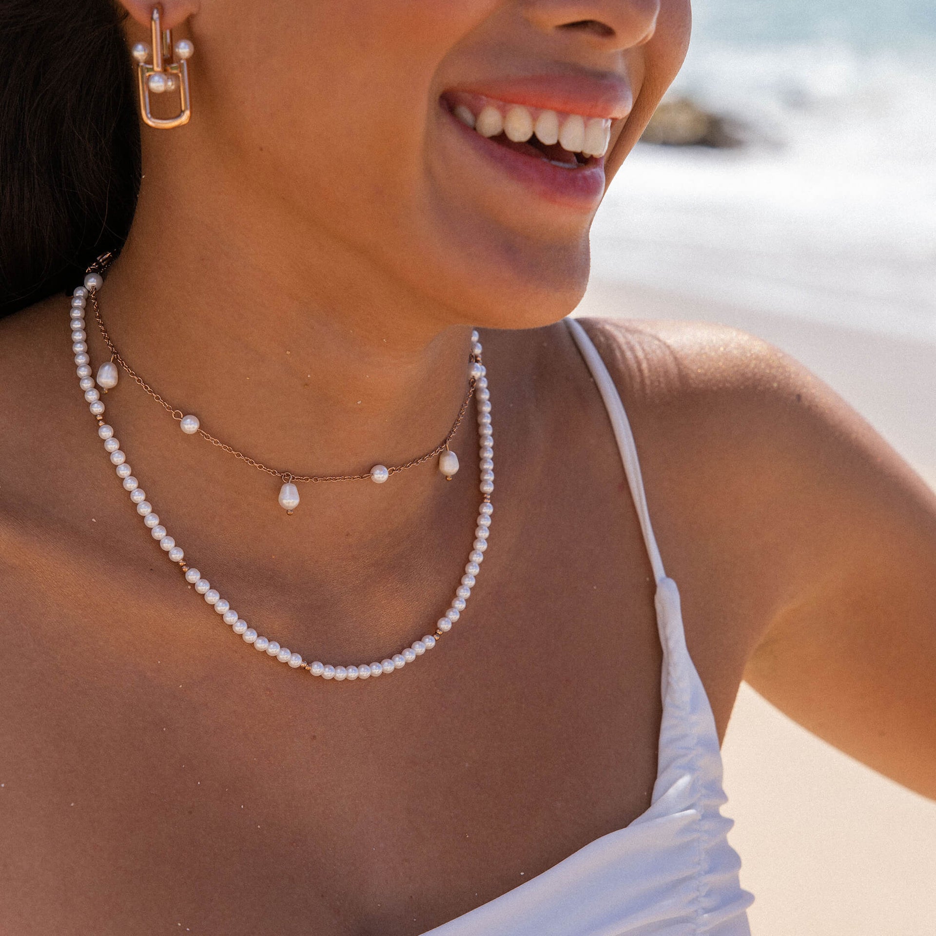 Zarte PURELEI Perlenkette und Ohrringe, elegant am Strand getragen, in warmem Licht.