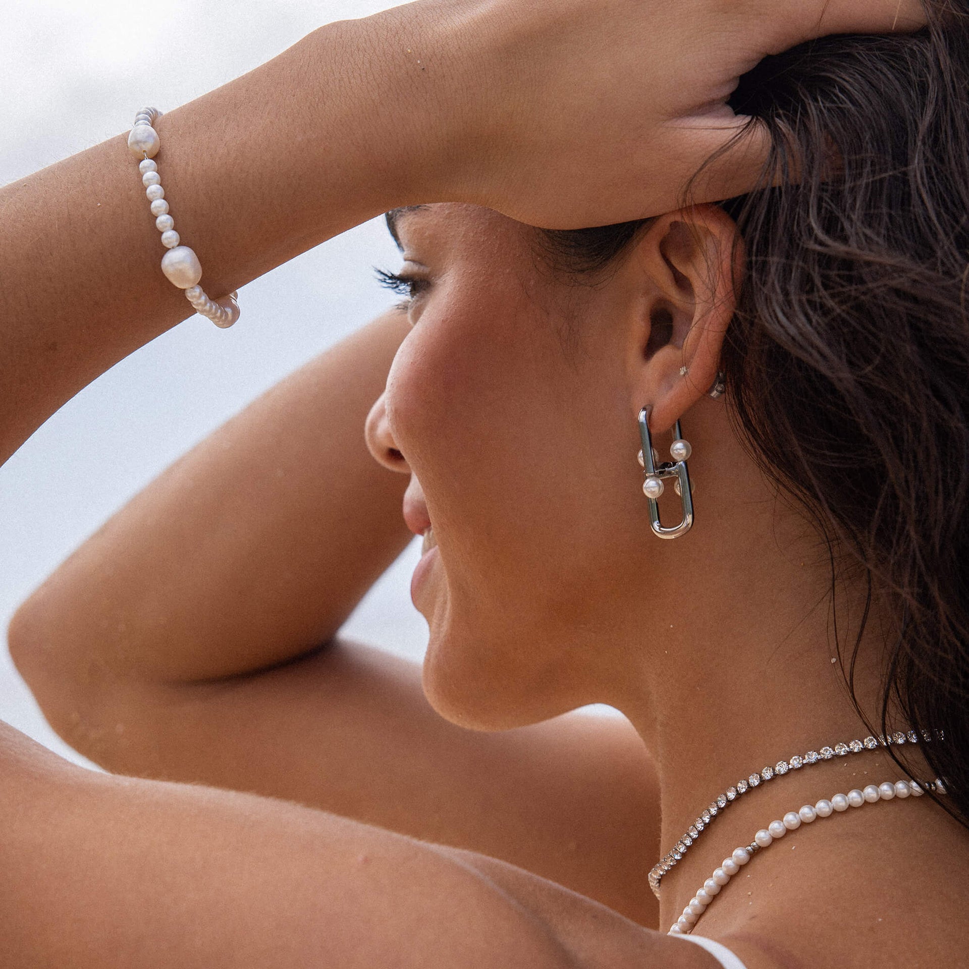 Silberne Ohrringe und Perlenarmband von PURELEI, elegant und feminin, am Handgelenk getragen.