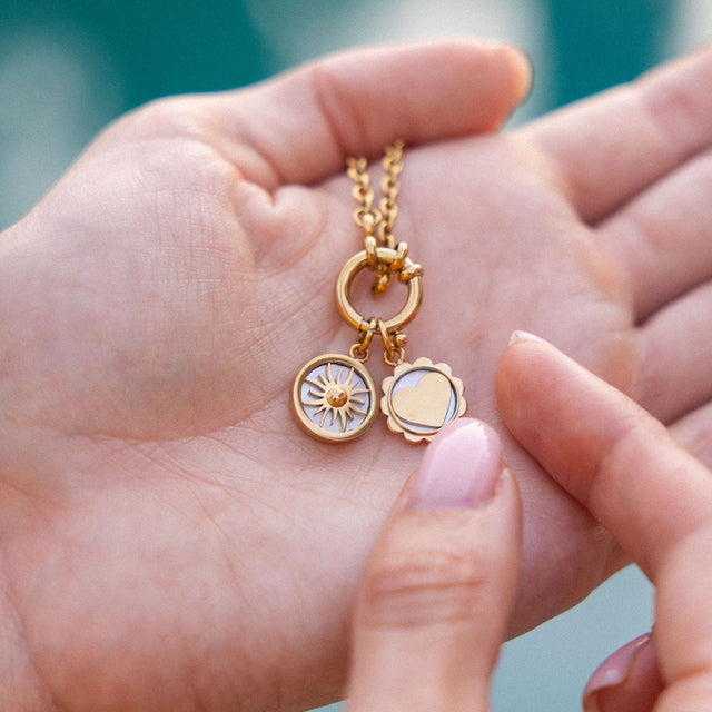 Roségoldene Kette mit Sonnen- und Herz-Anhängern, PURELEI, in sanfter Hand gehalten.