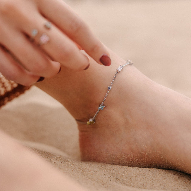 Silbernes Fußarmband mit zarten Details, getragen am Fuß im Sand, von PURELEI.