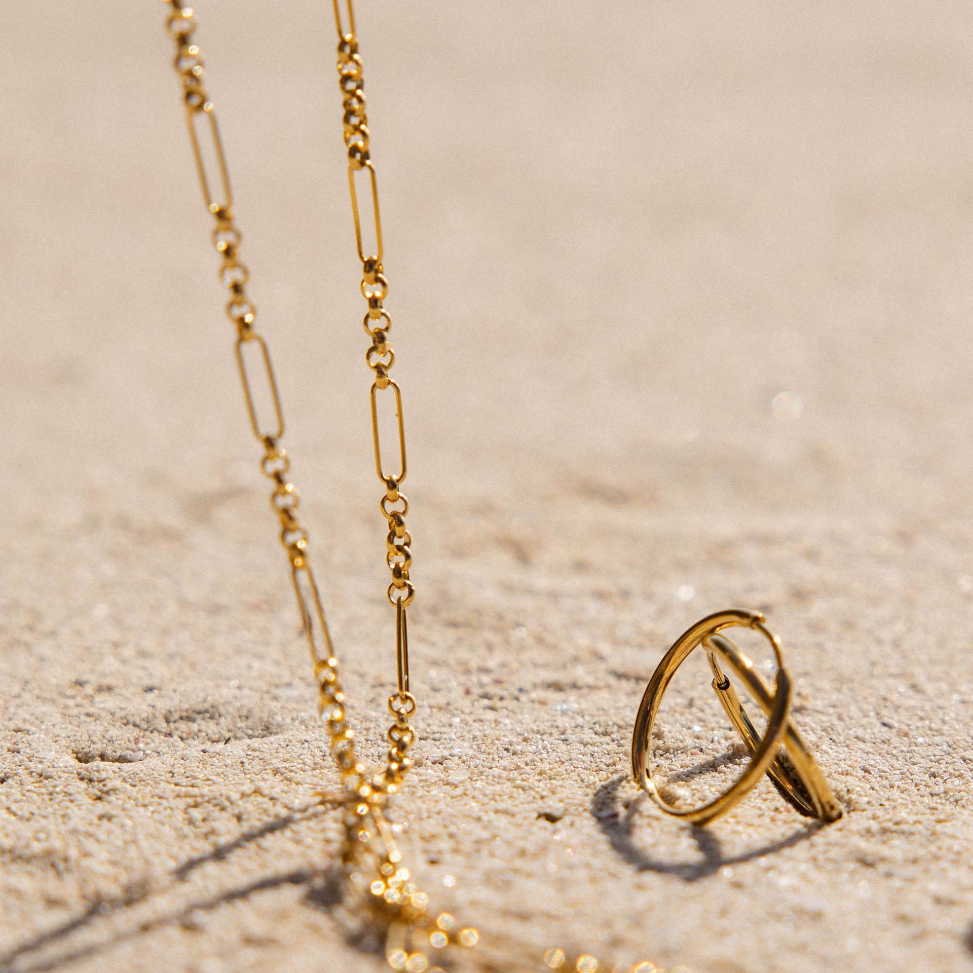 Goldene Kette und Ring auf Sand, PURELEI inspiriert von tropischer Eleganz.