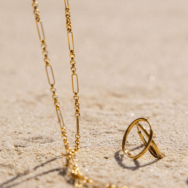 Goldene Kette und Ring auf Sand, PURELEI inspiriert von tropischer Eleganz.