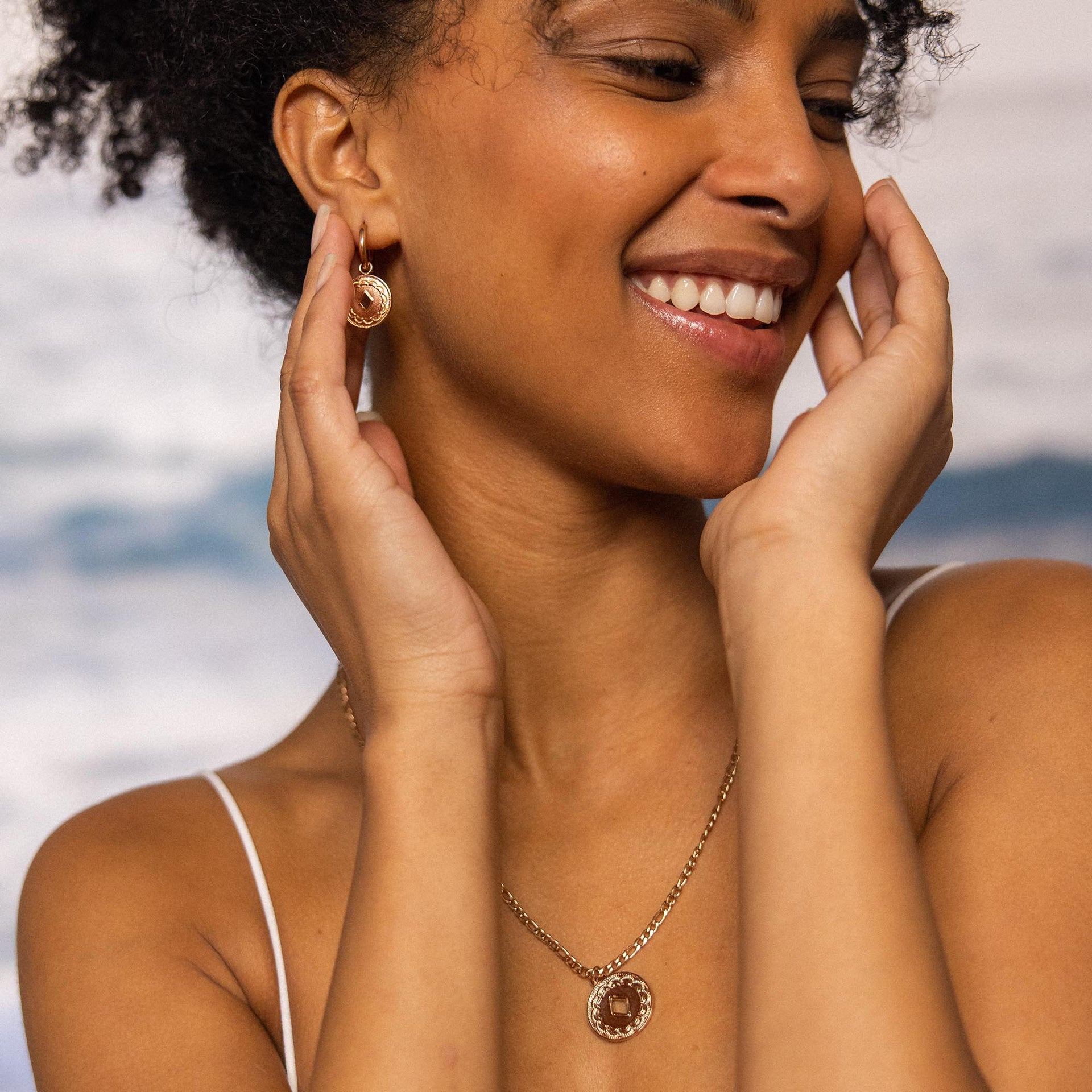 Roségoldene Ohrringe und Kette von PURELEI, elegant und strahlend, am Strand getragen.