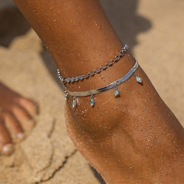 Silbernes Fußarmband mit Anhängern, getragen am Fuß im Sand, von PURELEI.