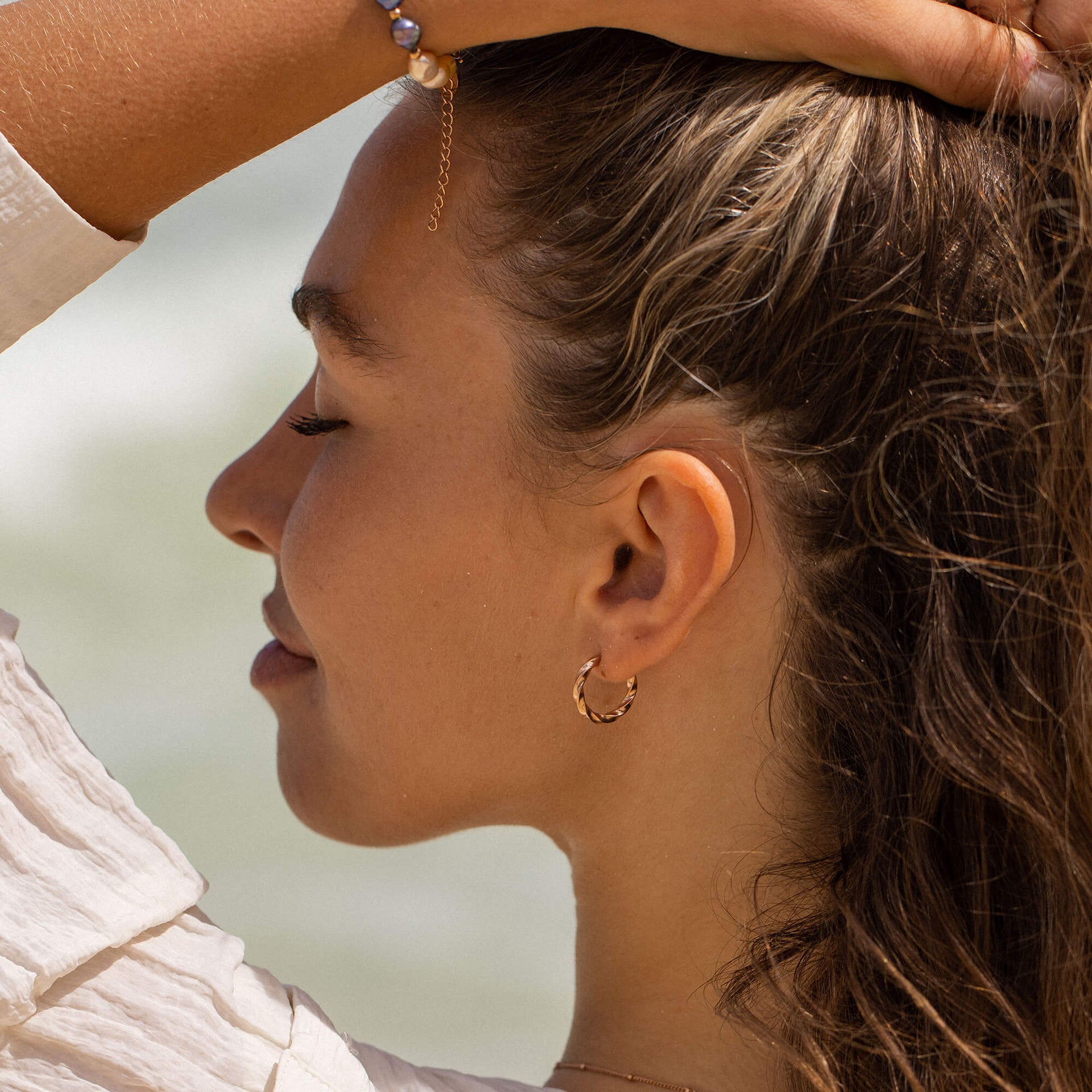 PURELEI Kelani Ohrringe aus goldvergoldetem Edelstahl mit gedrehtem Design getragen am Strand, feminin und elegant.
