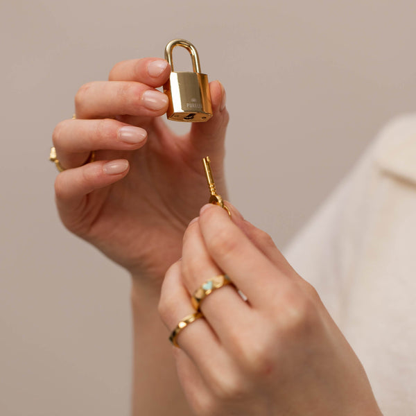 Roségoldenes Schloss von PURELEI in der Hand, Schlüssel wird gehalten, elegant und modern.